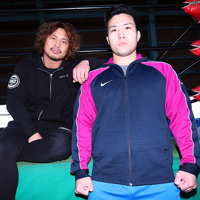 Nakajima Katsuhiko and Okada Kinya in casual training clothes in the Noah dojo. Nakajima has his hand on Okada's shoulder in a protective manner. 