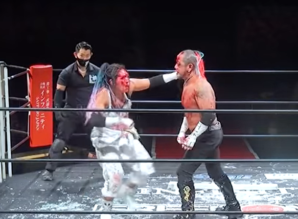 Rina and Kasai mid-match. There is glass on the mat and blood on both their faces. 