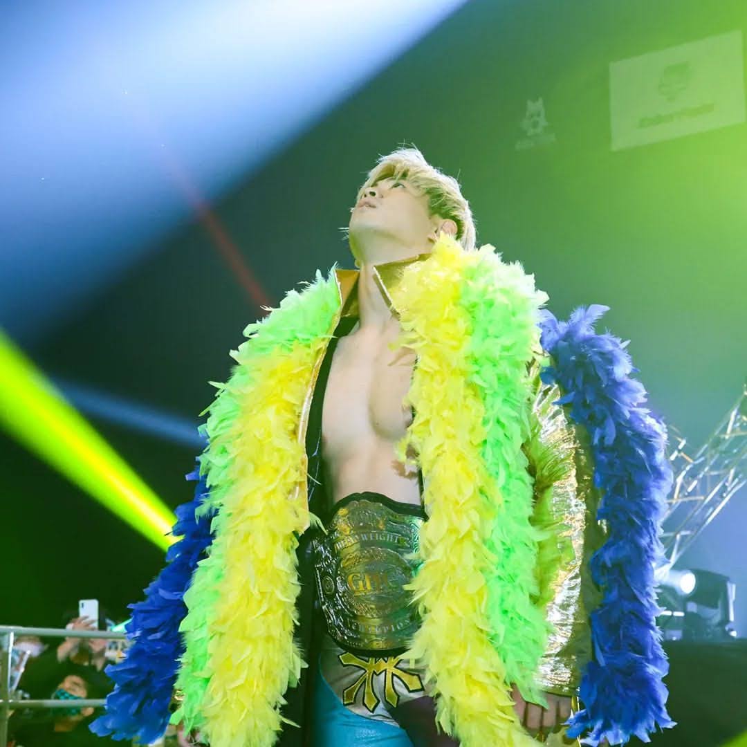 Kaito in gold and brightly coloured gear, wearing the title belt