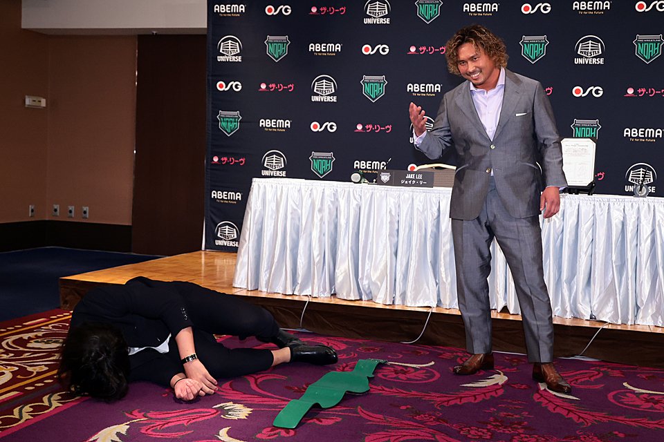 A photograph from the press conference ahead of the match. Nakajima poses in his suit whilst Jake lies on the floor, downed by Nakajima's slap.  